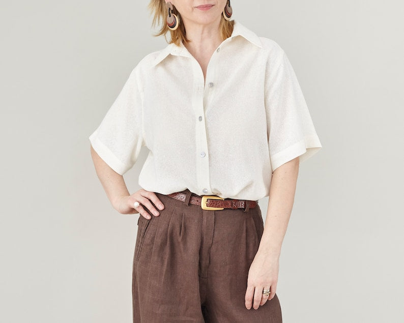 Person wearing a short sleeve oversized shirt with mother of pearl buttons in la lightweight off white fabric, slightly sheer.