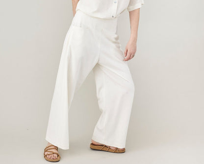 Person wearing white wide leg pants and a white shirt on a plain background