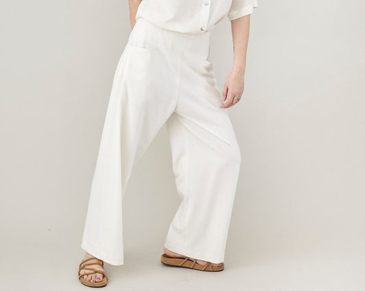Person wearing white wide leg pants and a white shirt on a plain background