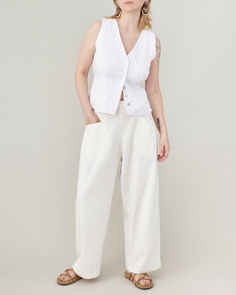 Full-length portrait of a model wearing handmade raw silk wide-leg trousers in natural ivory, styled with a white button-down vest for an elegant, minimalist summer outfit.