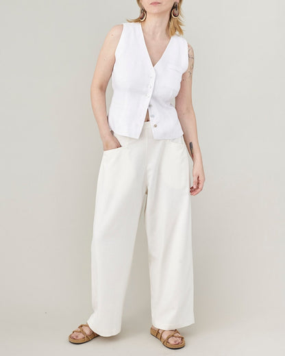 Full-length portrait of a model wearing handmade raw silk wide-leg trousers in natural ivory, styled with a white button-down vest for an elegant, minimalist summer outfit.