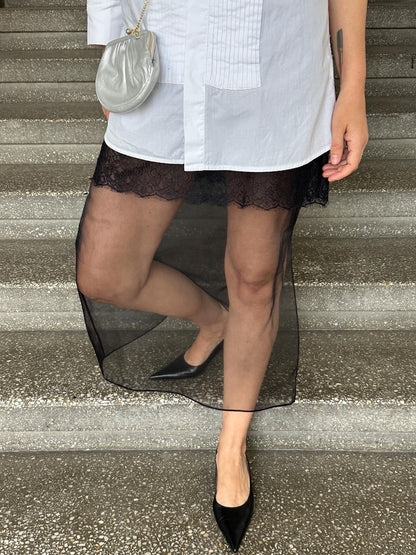 Sheer black silk organza skirt layered over black lace slip, styled with a long white shirt and pointed black heels