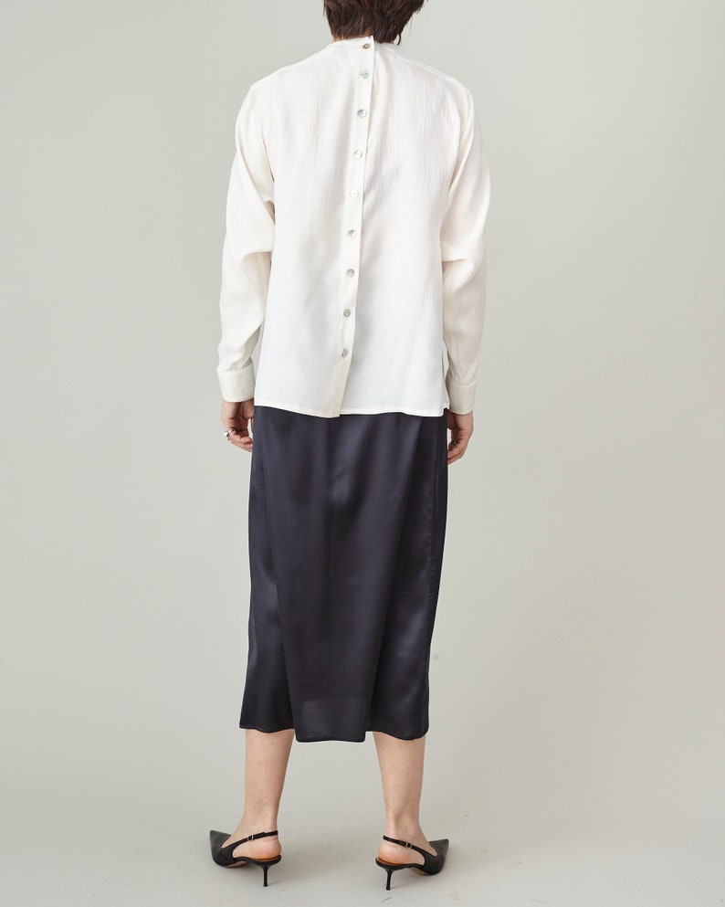 Person wearing a white shirt with back buttons and black skirt on a plain background