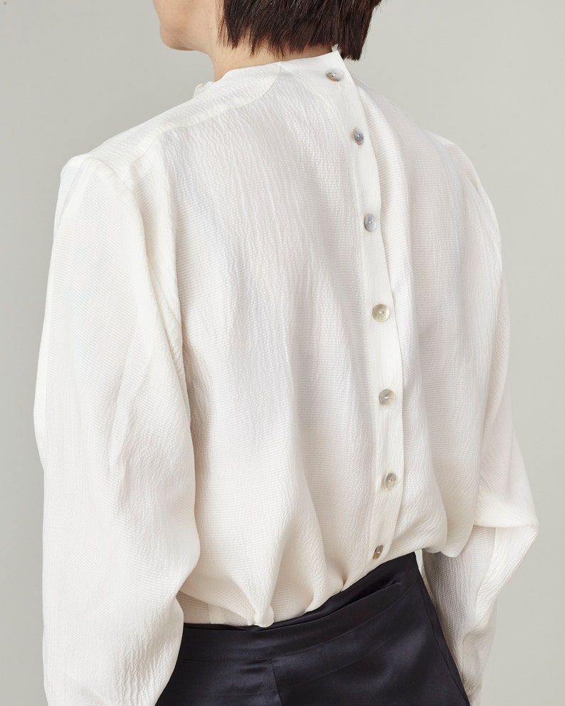 Person wearing a white blouse with back mother of pearl buttons a plain background