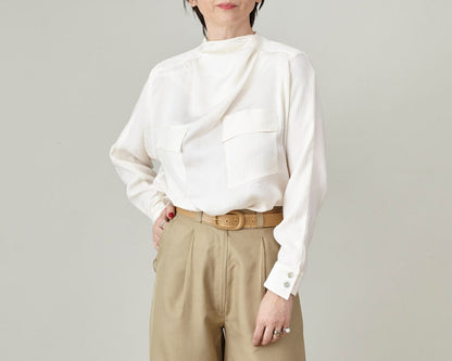 Person wearing a white blouse and beige pants against a plain background