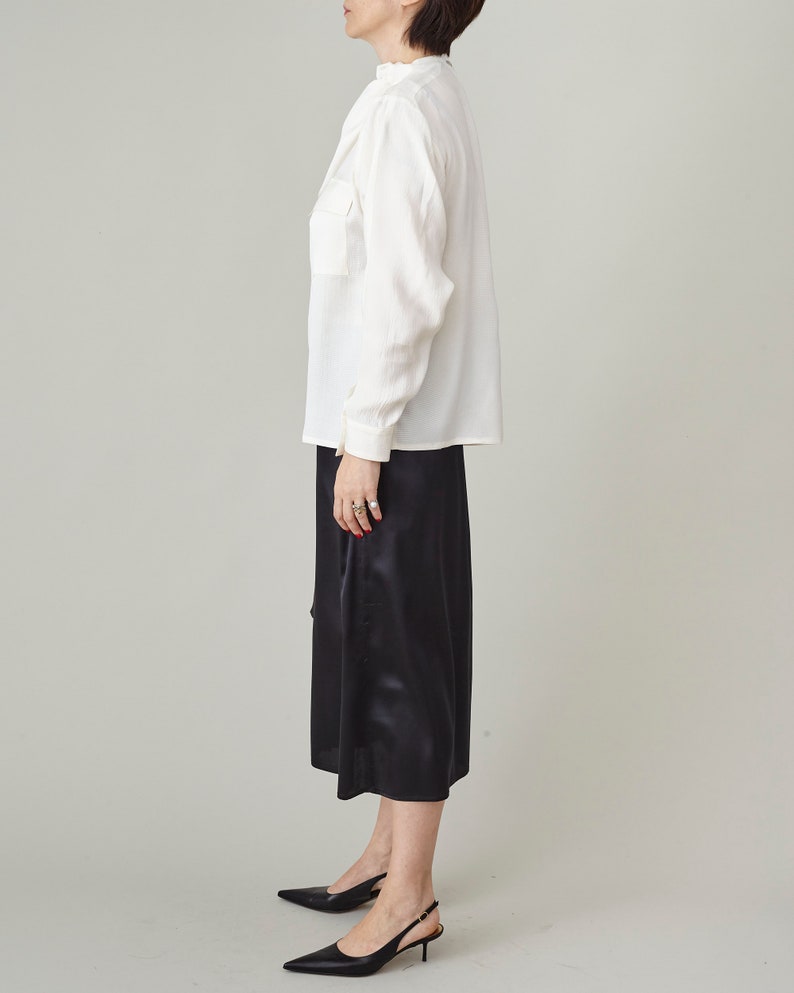 Person wearing a white blouse and black pants on a plain background