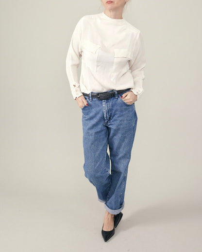 Person wearing a white blouse and blue jeans on a plain background