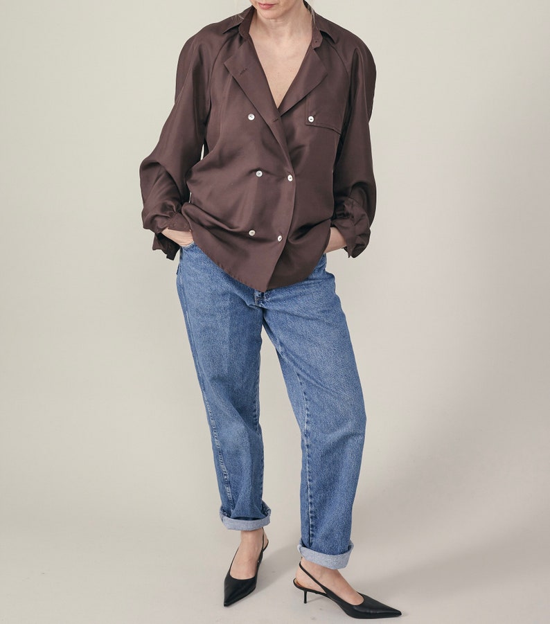 Person wearing a brown button-up shirt and blue jeans on a plain background