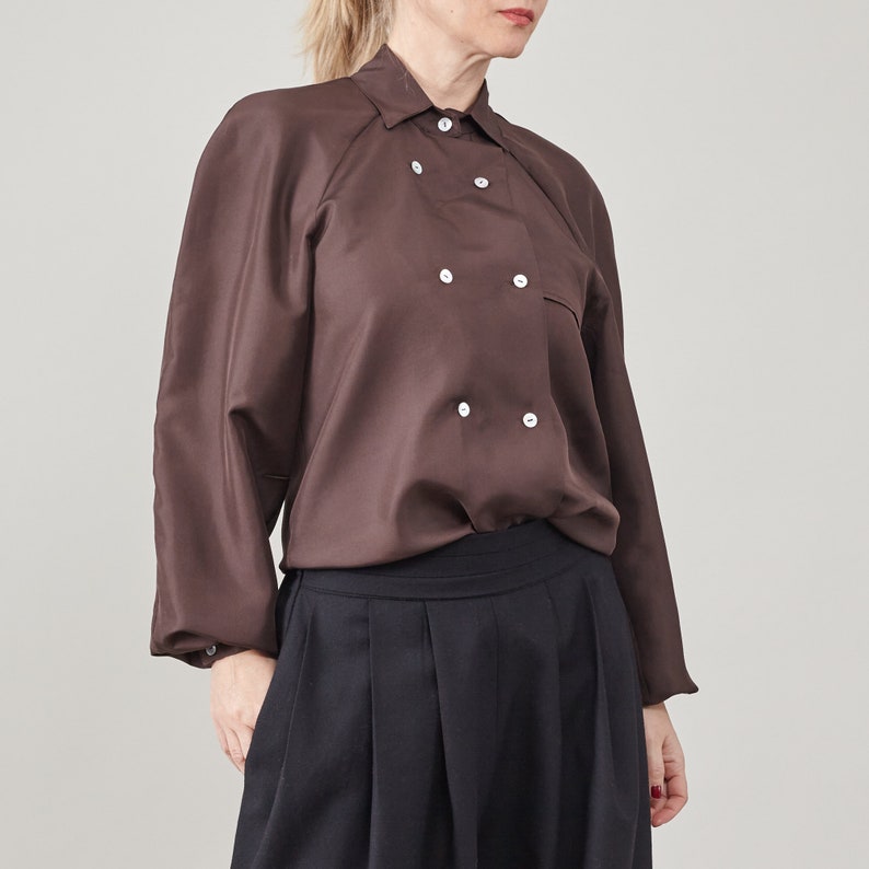 Person wearing a brown blouse with double breasted mother of pearl buttons on a plain background