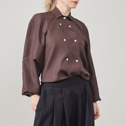 Person wearing a brown blouse with double breasted mother of pearl buttons on a plain background