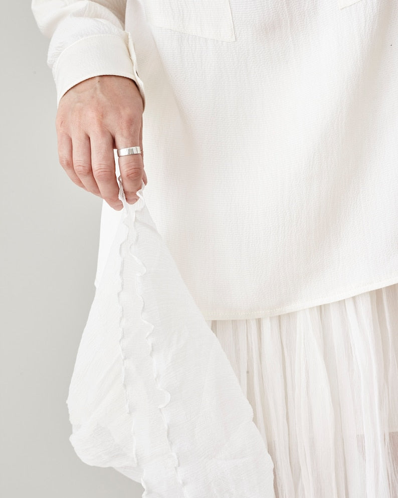 Person wearing a white silk chiffon skirt with a ruffled hem on a plain background