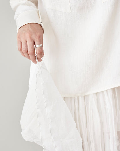 Person wearing a white silk chiffon skirt with a ruffled hem on a plain background