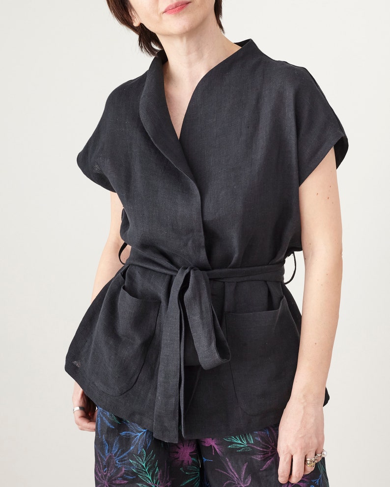 Person wearing a black sleeveless jacket with a belt on a plain background