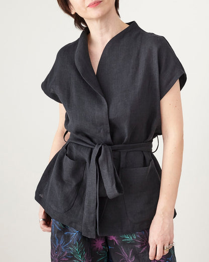 Person wearing a black sleeveless jacket with a belt on a plain background