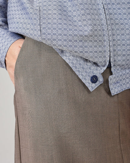 Close-up of a person wearing a blue patterned jacket and greige skirt with pockets on a light gray background