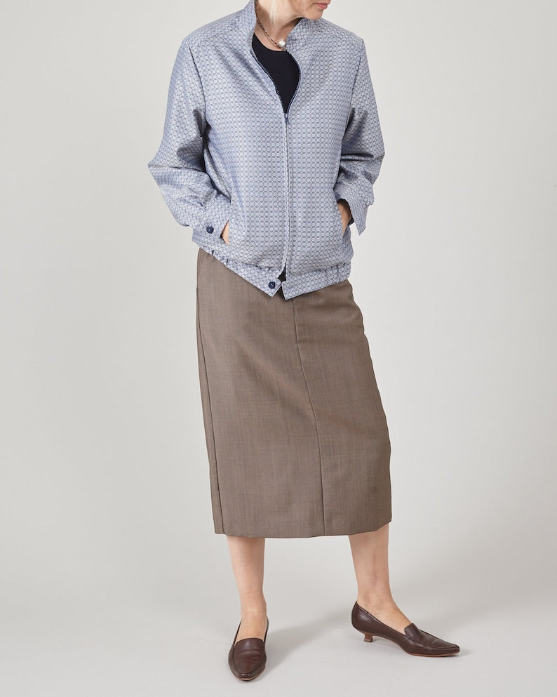 Person wearing a blue patterned jacket, greige skirt and brown kitten heels on a white background