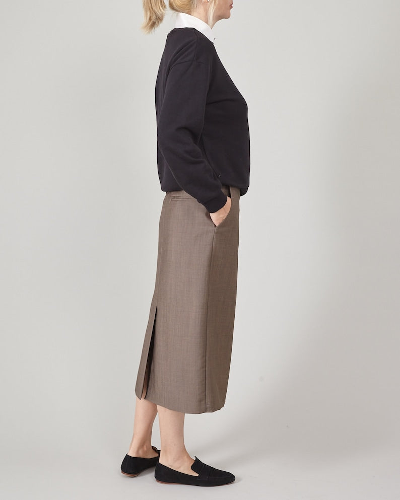 Person wearing a black sweatshirt, brown skirt and loafers on a plain background