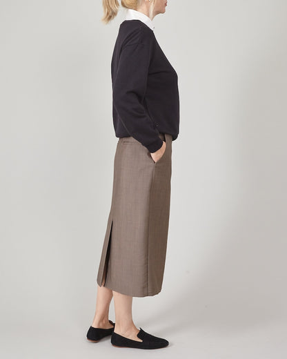 Person wearing a black sweatshirt, brown skirt and loafers on a plain background