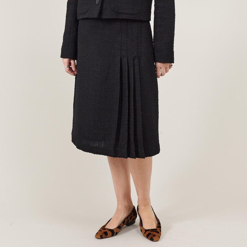 Person wearing a black skirt with a matching top on a plain background