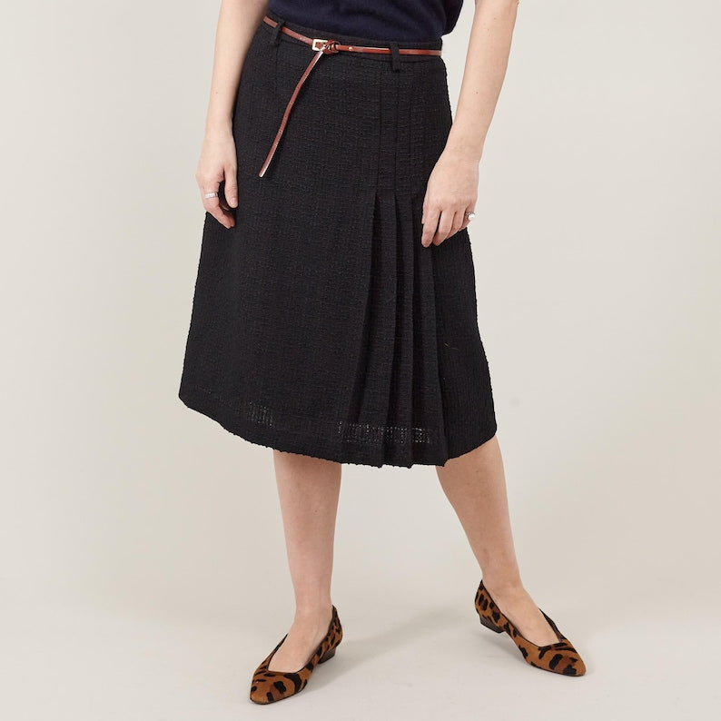 Person wearing a black skirt with a belt on a beige background