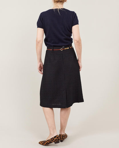 Person wearing a navy shirt and black skirt on a plain background