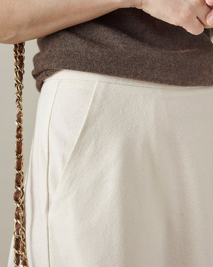 Close-up of a person wearing a brown sweater and white skirt