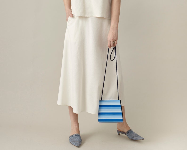 Person wearing a white midi skirt holding a blue and white striped handbag against a plain background