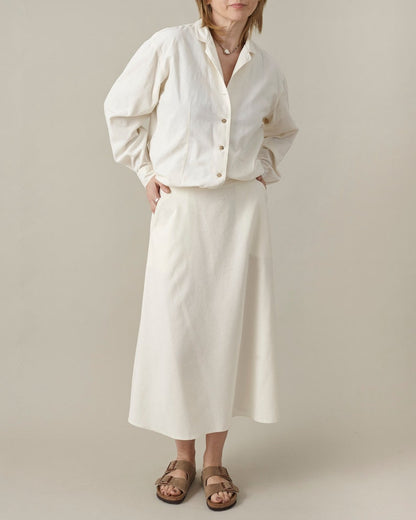 Person wearing a white shirt and skirt with rolled-up sleeves on a plain background