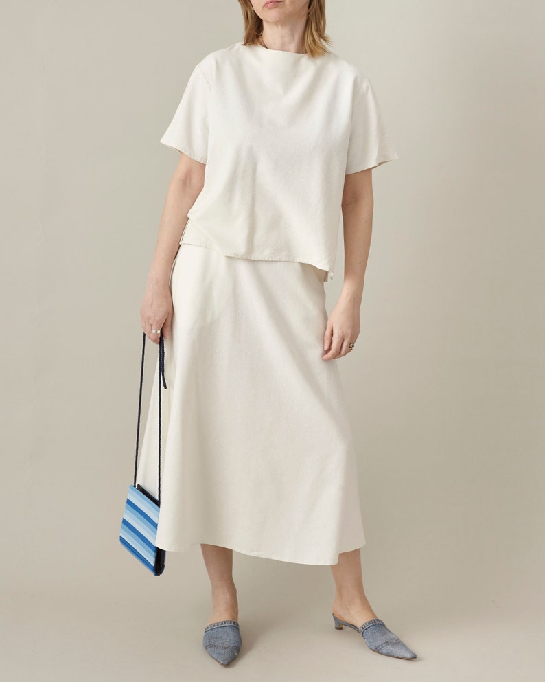 Person wearing a white outfit holding a striped bag against a plain background