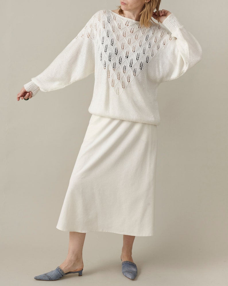 Woman wearing a white outfit with a patterned top and plain skirt on a neutral background