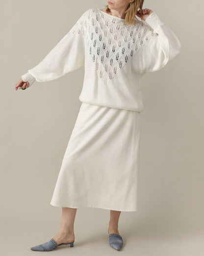 Woman wearing a white outfit with a patterned top and plain skirt on a neutral background