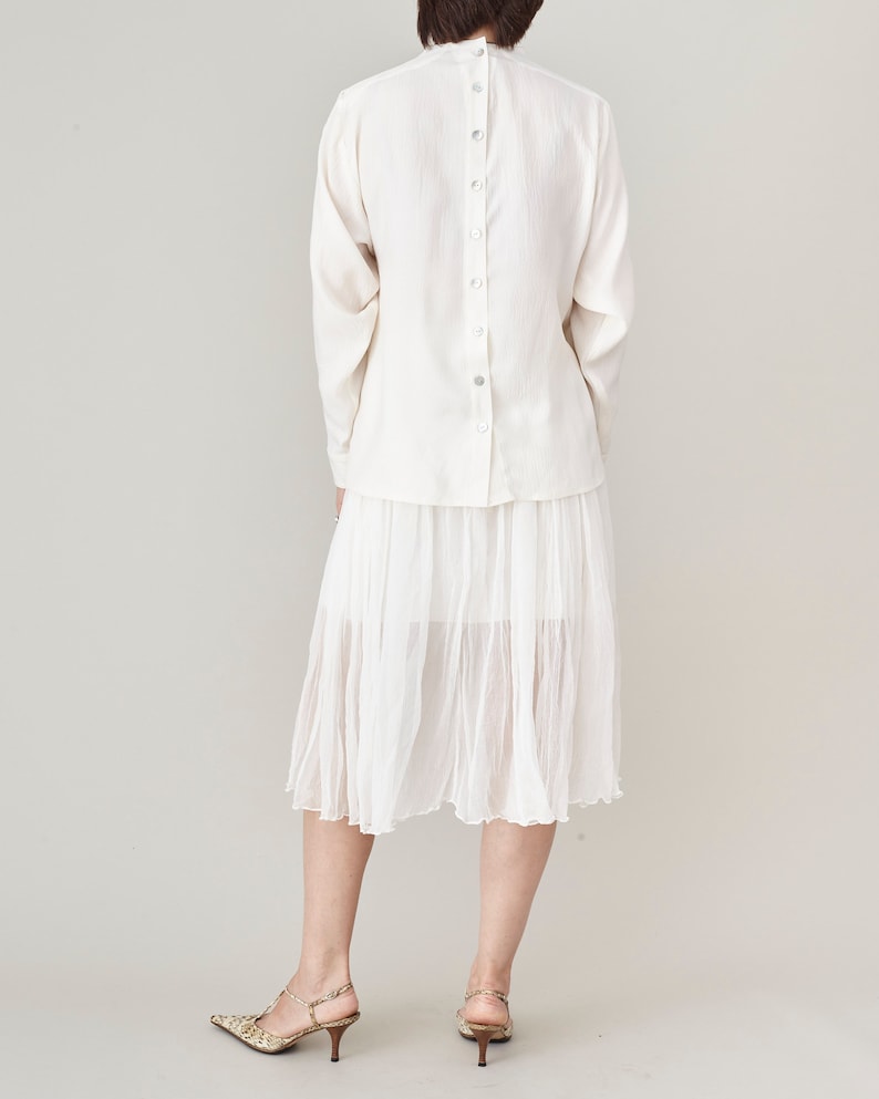 Person wearing a all white outfit with back button blouse and silk chiffon midi skirt, paired with snake print heels.