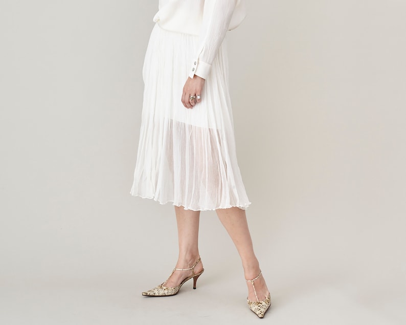 Person wearing a white silk chiffon midi skirt with thigh long underlay and high-heeled animal print shoes on a plain background