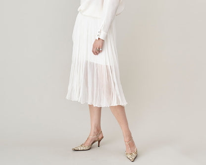 Person wearing a white silk chiffon midi skirt with thigh long underlay and high-heeled animal print shoes on a plain background