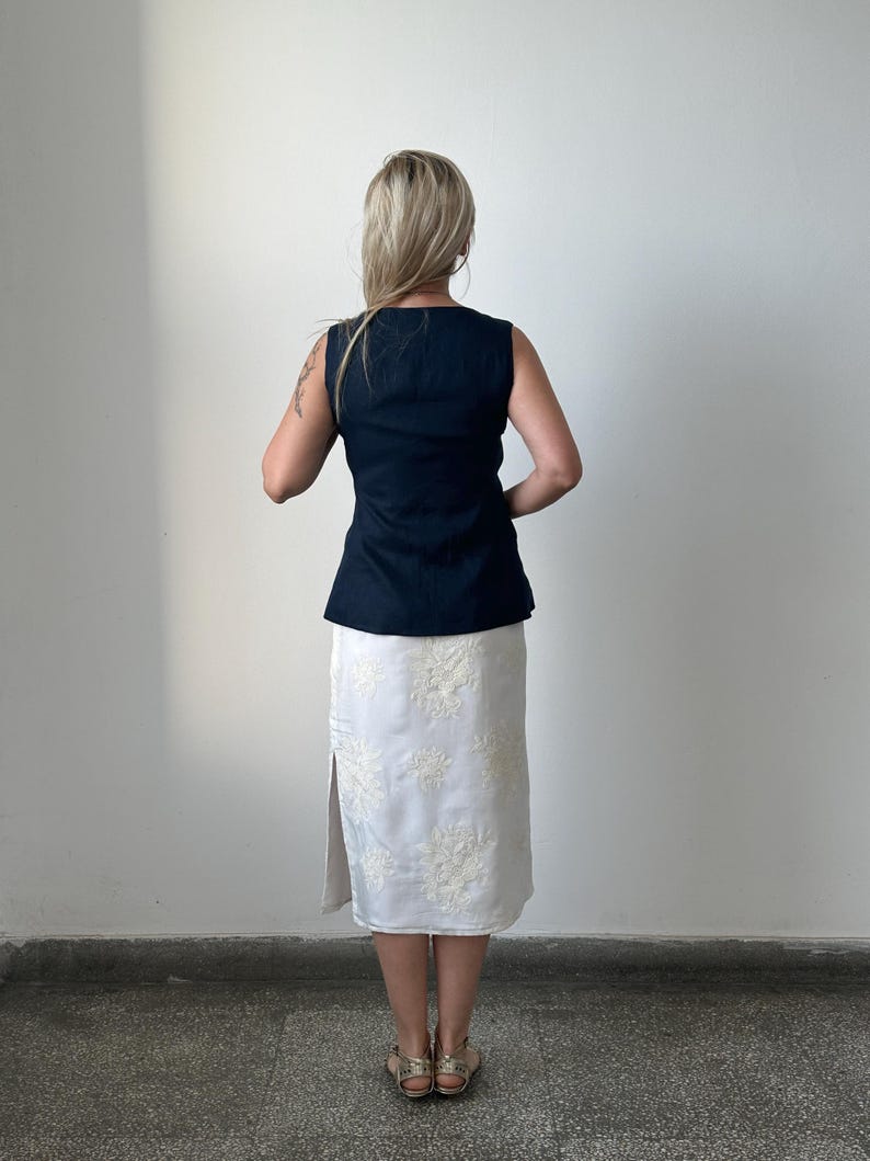 Person wearing a navy top and white lace skirt against a plain background