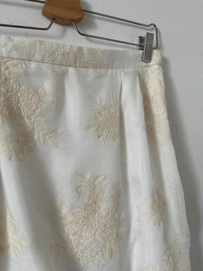 White skirt with ivory embroidery on a hanger against a white wall