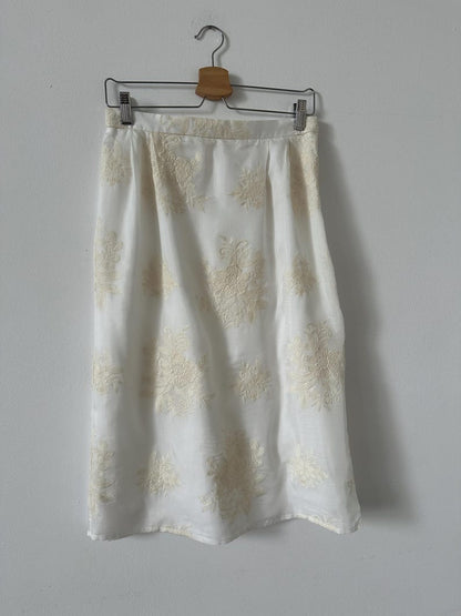 White skirt with ivory floral embroidery on a hanger against a gray wall