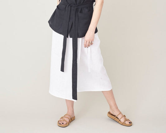 Person wearing a black top and white skirt with a belt on a plain background