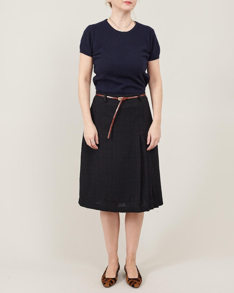 Person wearing a navy shirt and black skirt with a belt on a plain background
