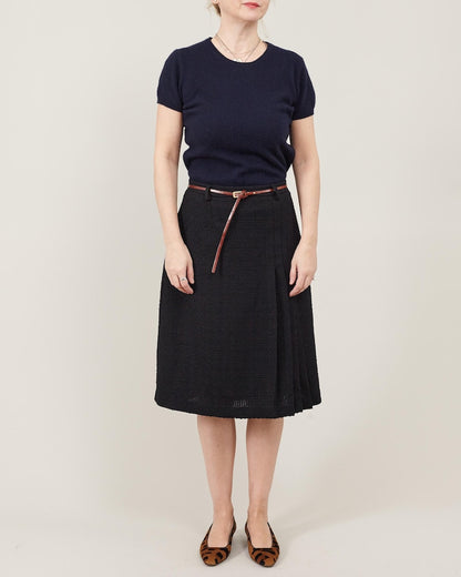 Person wearing a navy shirt and black skirt with a belt on a plain background