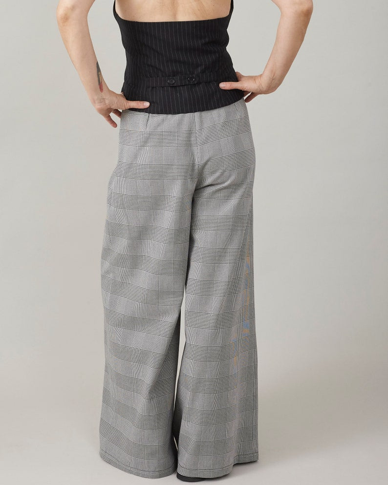 Person wearing an open back vest and gray checkered pants on a plain background