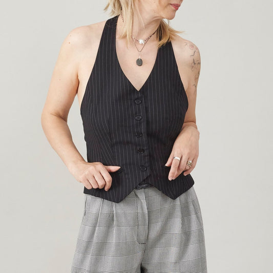 Person wearing a black pinstripe vest with plaid pants on a light gray background