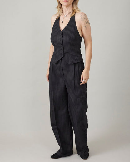 Woman wearing a black pinstripe jvest and matching trousers on a plain background