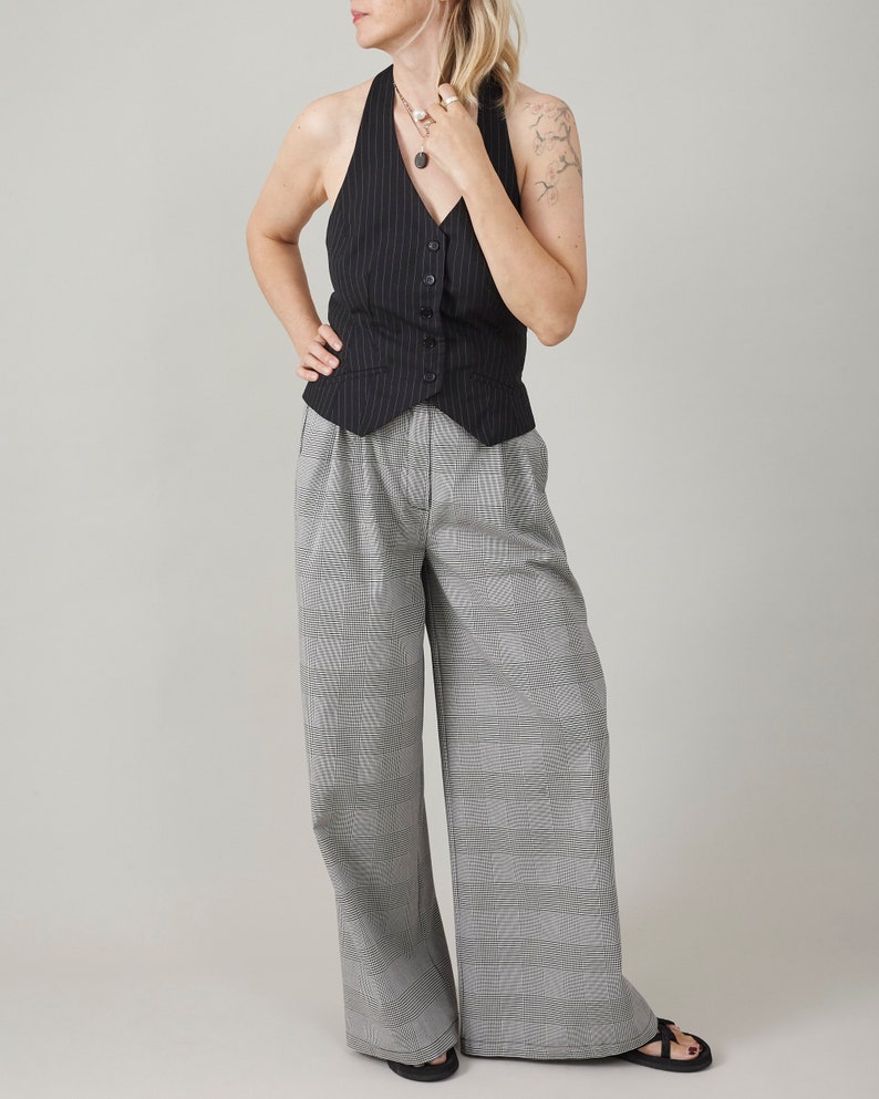 Woman wearing a pinstripe vest and gray plaid pants against a plain background