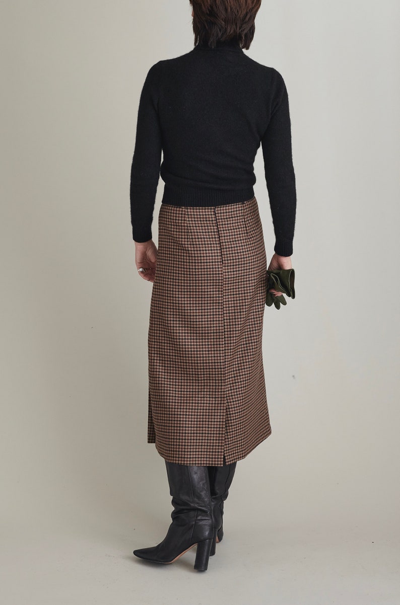 Person wearing a black turtleneck and brown checkered skirt on a plain background