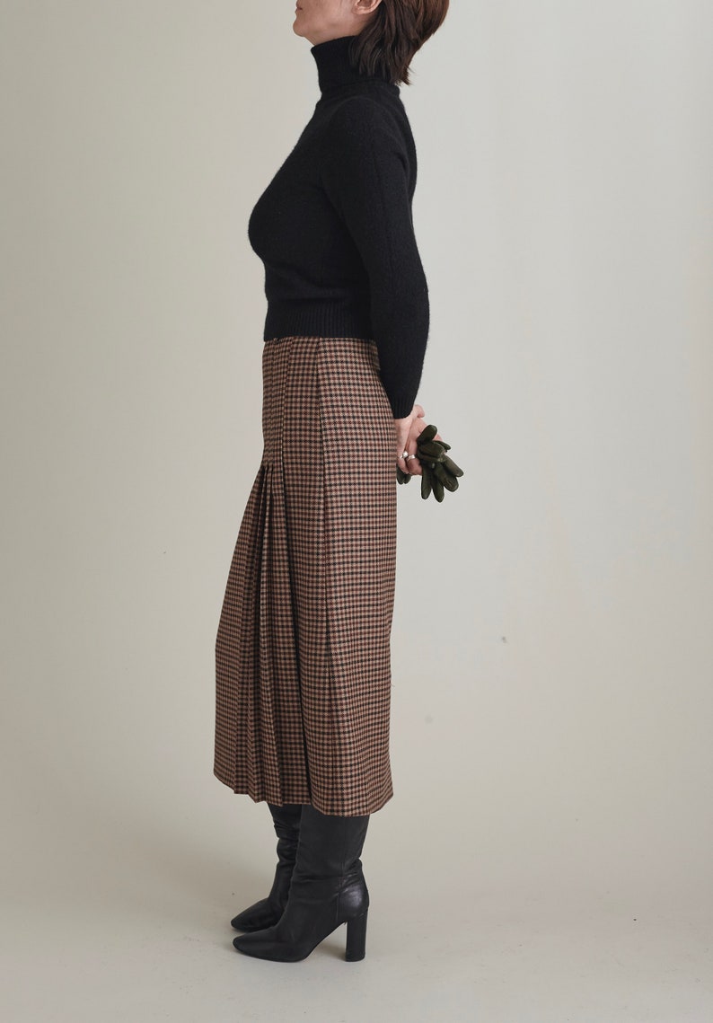 Person wearing a black turtleneck and brown plaid skirt on a plain background